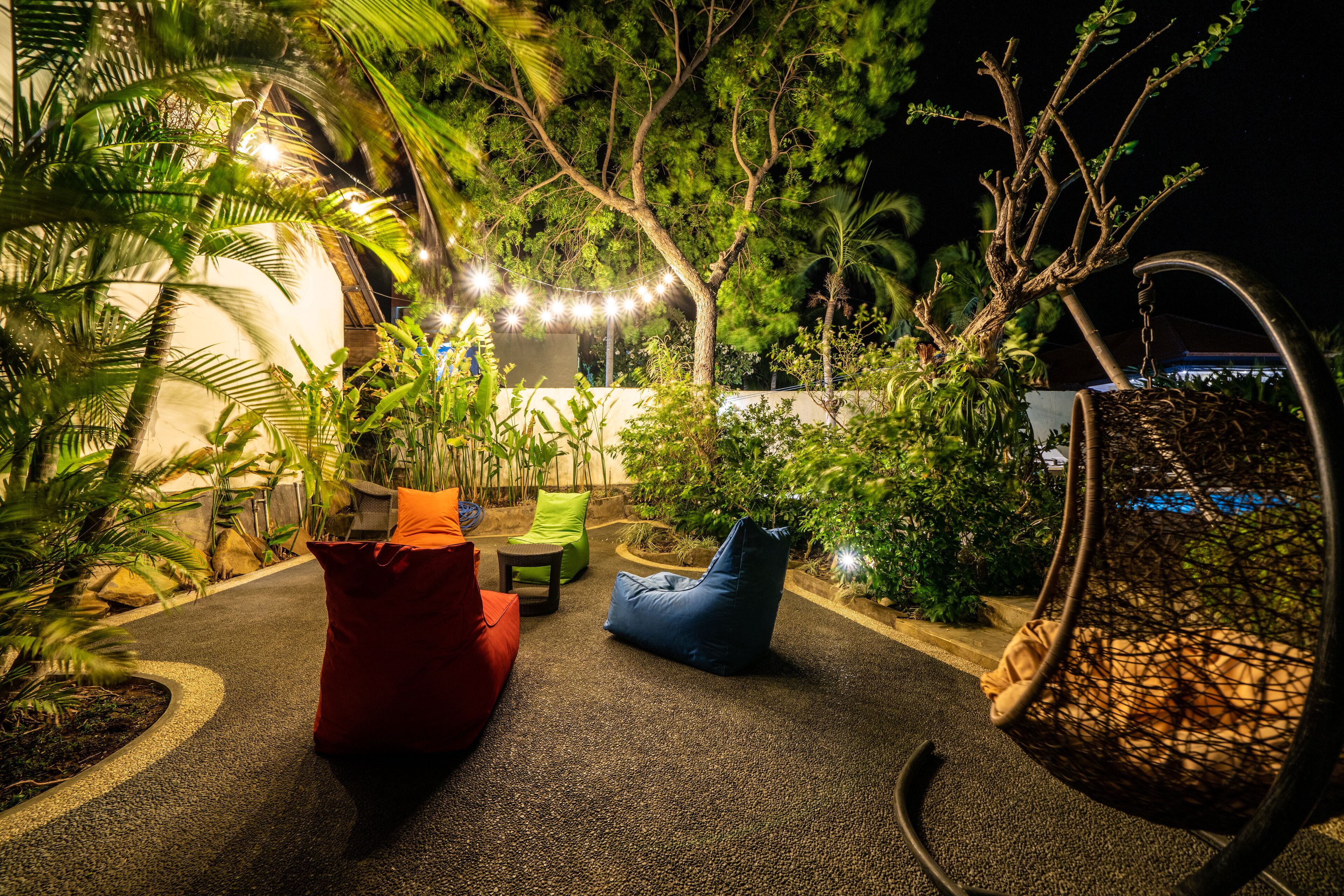 An outdoor seating area with a swing chair, a red bean bag, and a blue bean bag.