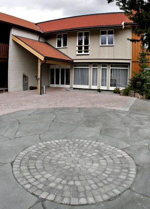 A building with a circular courtyard paved with stone tiles, large windows, and a red-tiled roof. - Søstrene Storaas Hotell (Kongsberg)