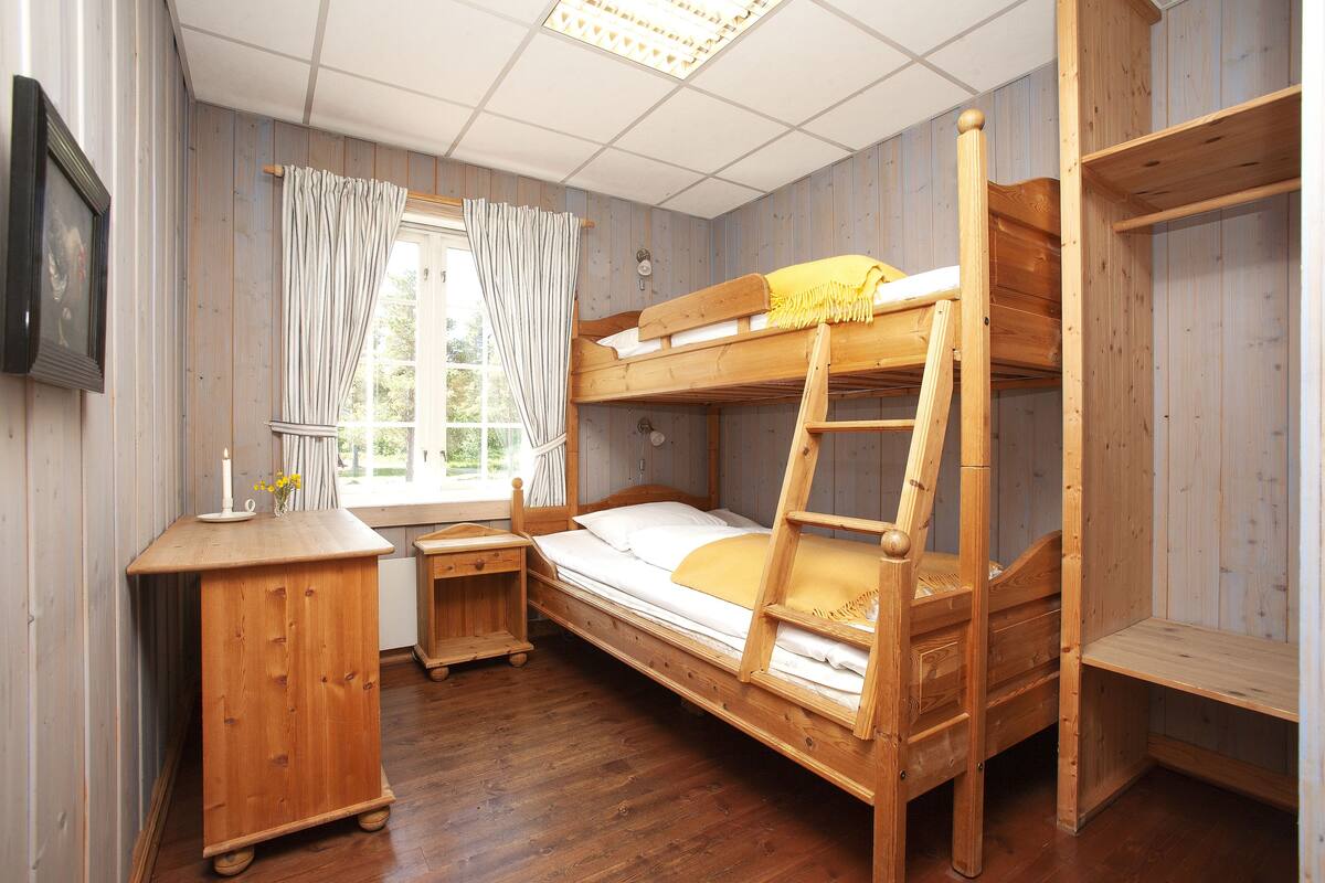 Habitación con literas de madera, un escritorio y una ventana con cortinas.