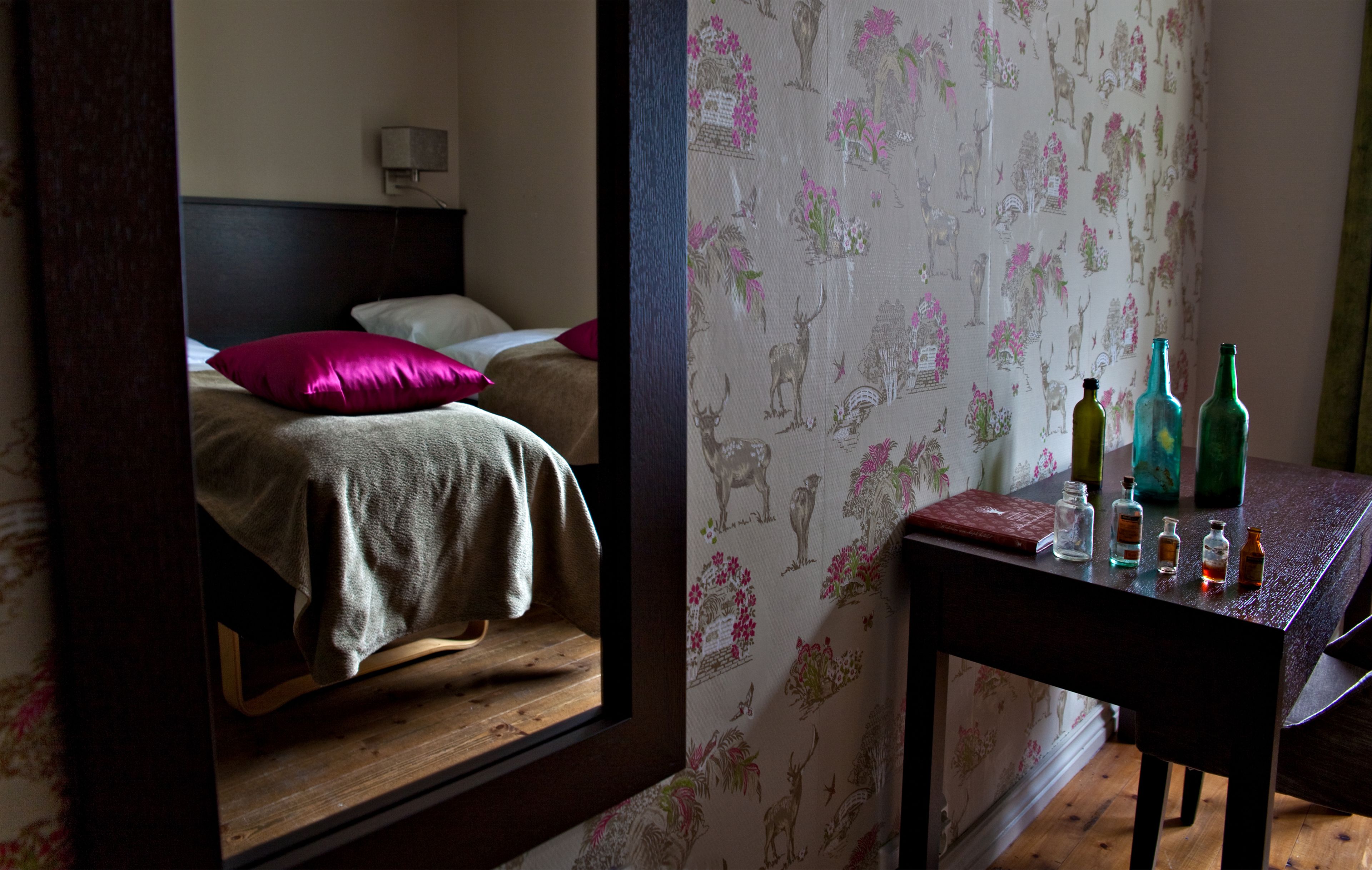 A bedroom with a bed, a nightstand, and a mirror reflecting the room.