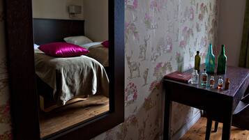 A bedroom with a bed, a nightstand, and a mirror reflecting the room.