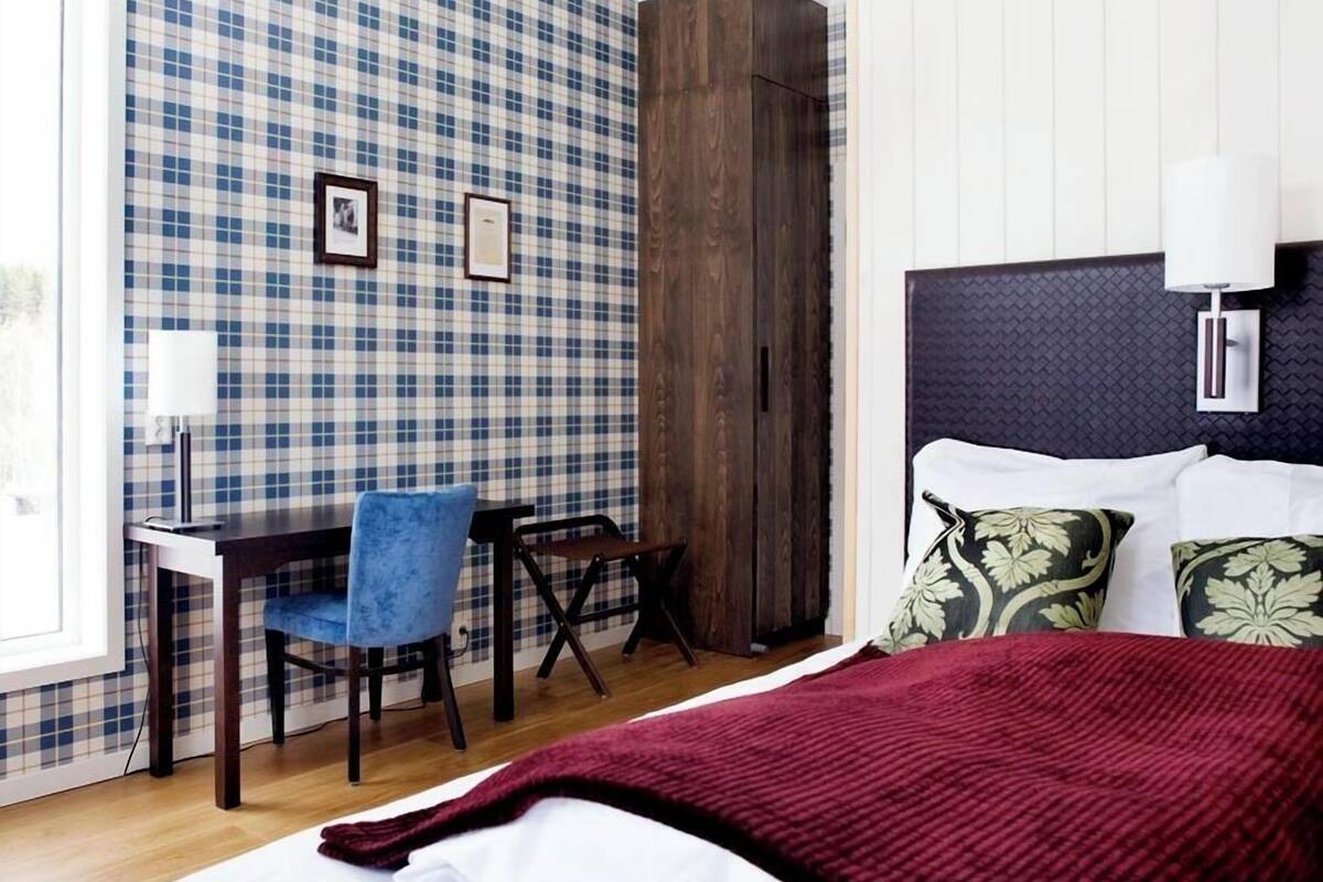 Un dormitorio con pared a cuadros, una cama con cabecera oscura y un escritorio con silla.