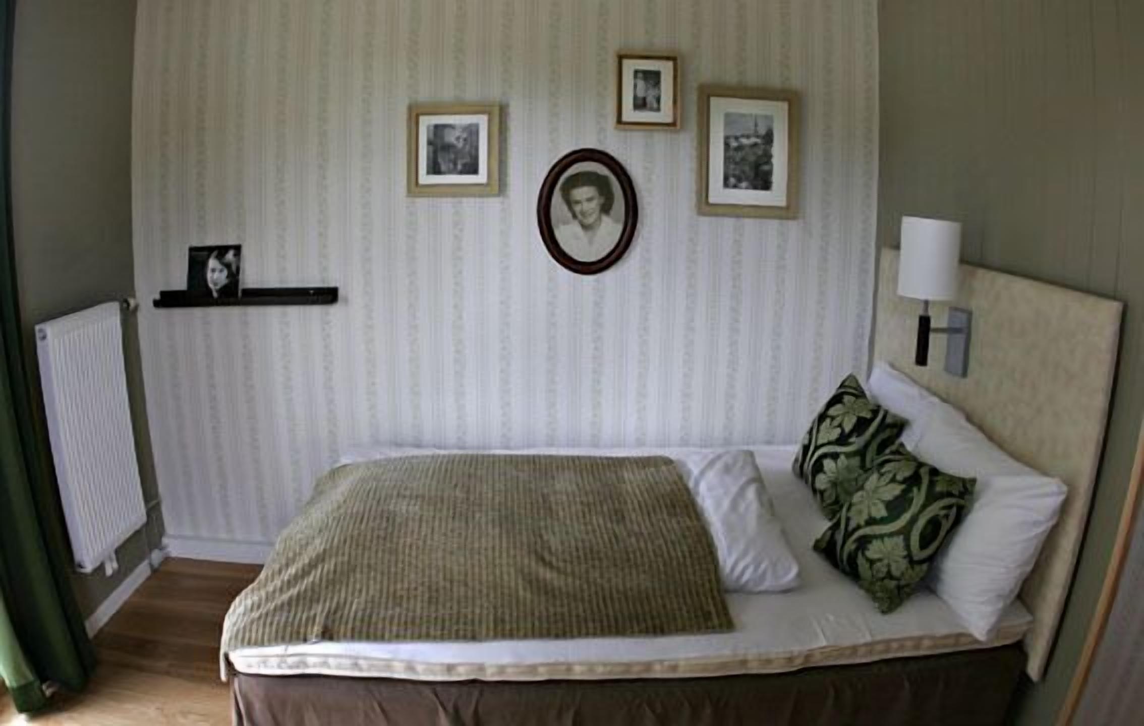 Een slaapkamer met een bed, een radiator en lijstjes met foto's aan de muur.