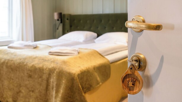 Una cama con cabecera verde, un pomo de madera en la puerta y una cerradura con un llavero con forma de árbol.