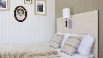 Una cama bien tendida con sábanas blancas y almohadas a rayas, una manta beige y una lámpara de pared.