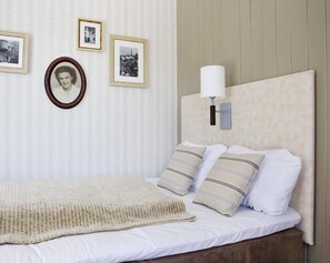 Una cama bien tendida con sábanas blancas y almohadas a rayas, una manta beige y una lámpara de pared.