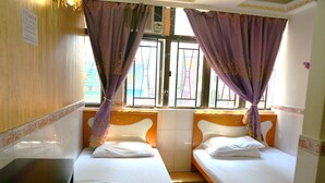 Une chambre avec deux lits, une fenêtre ornée de rideaux violets et une tête de lit en bois.