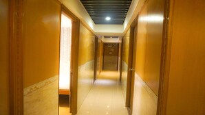 Un long couloir étroit, avec des portes des deux côtés, qui mène à différentes pièces. Les murs sont d’un jaune chaleureux et le sol est carrelé.