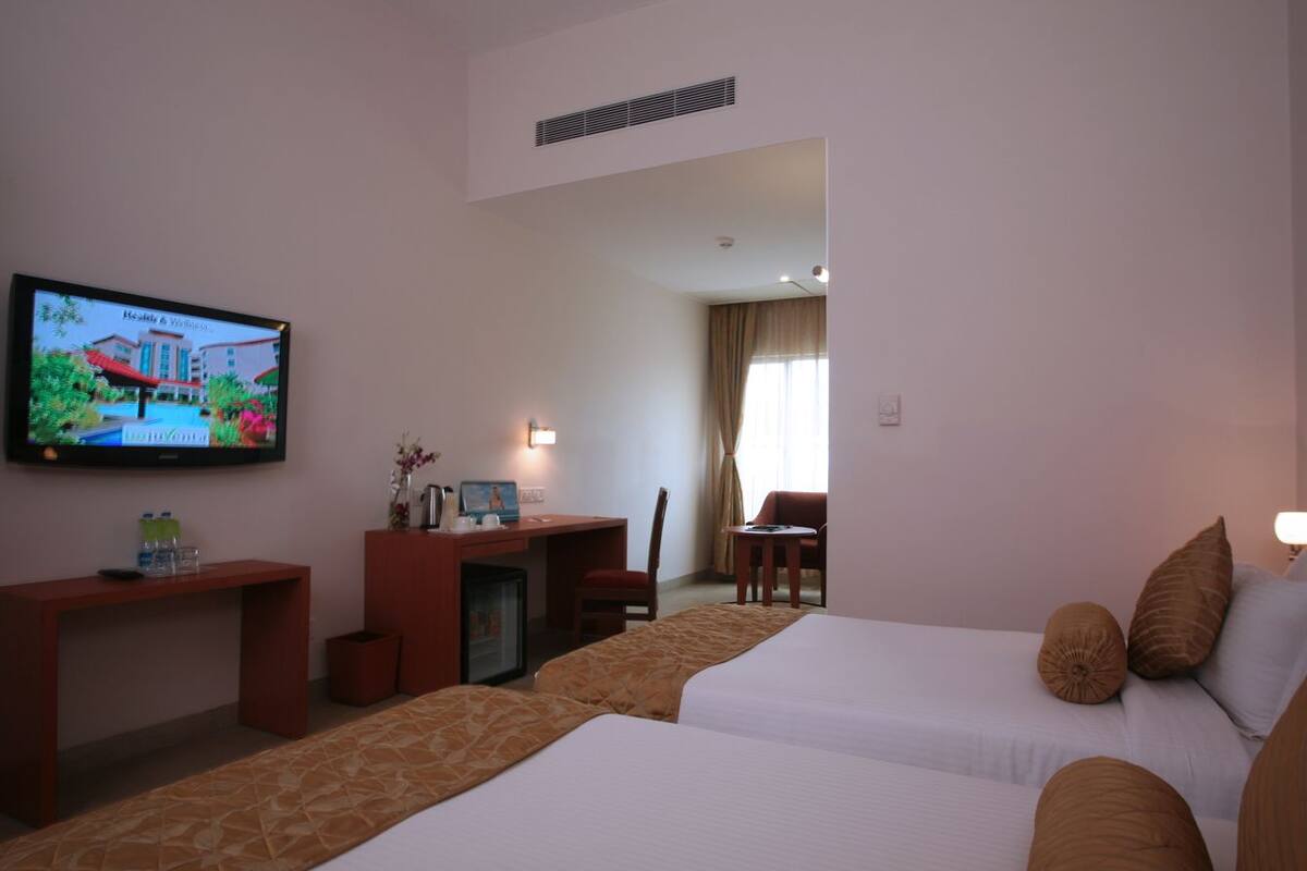 Habitación de hotel con dos camas, un escritorio, un televisor y vista al exterior del hotel.
