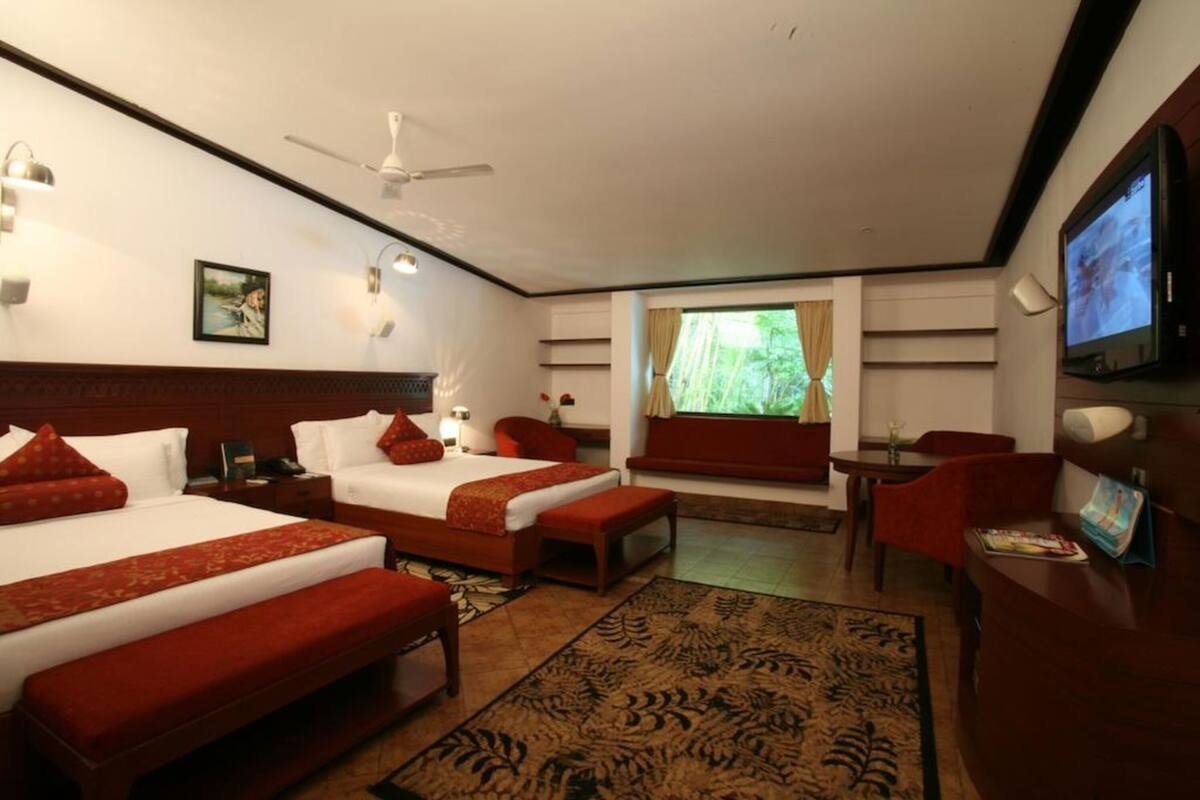 Habitación de hotel con dos camas, un escritorio, televisor, ventilador de techo y ventana con cortinas.
