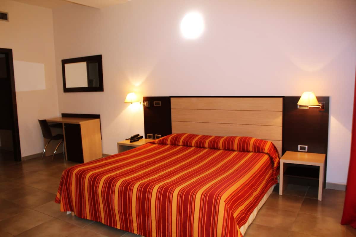 Ein Hotelzimmer mit einem großen Bett, zwei Nachttischen, einem Schreibtisch und einem Sessel.