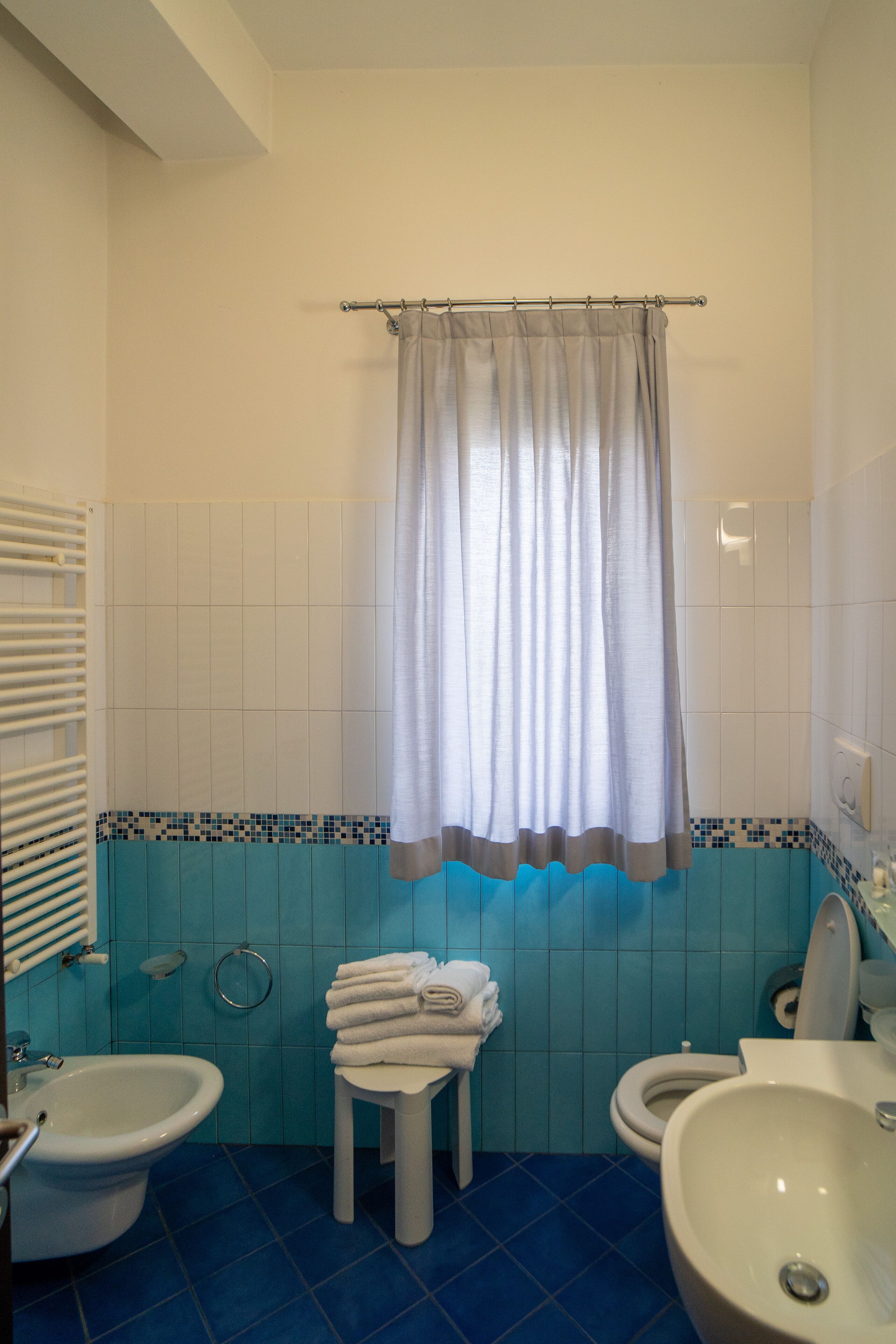 A bathroom with a bidet, toilet, and sink, featuring blue tiles and a curtain.