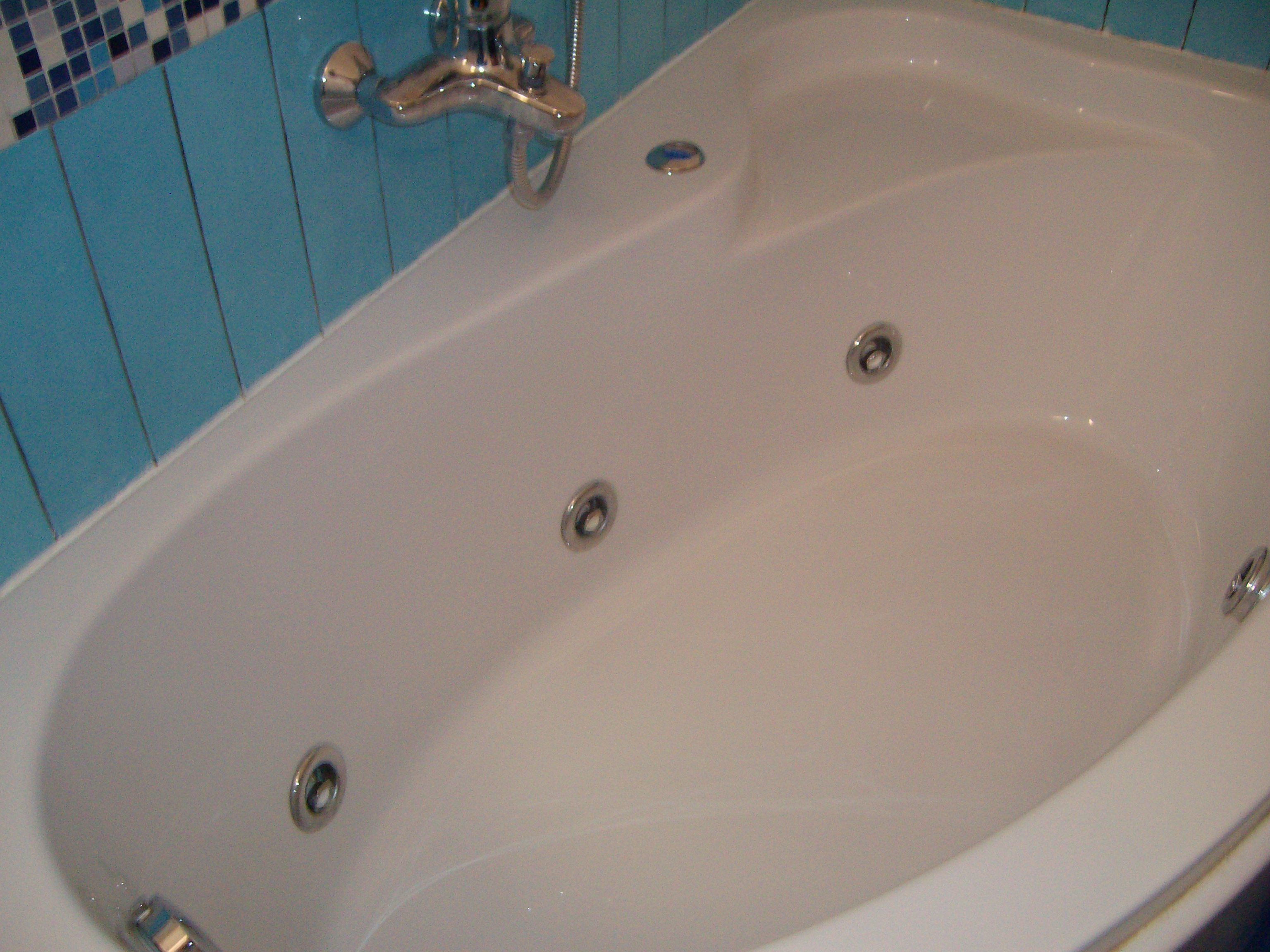 Eine weiße Badewanne mit Chromarmatur und drei Abläufen.