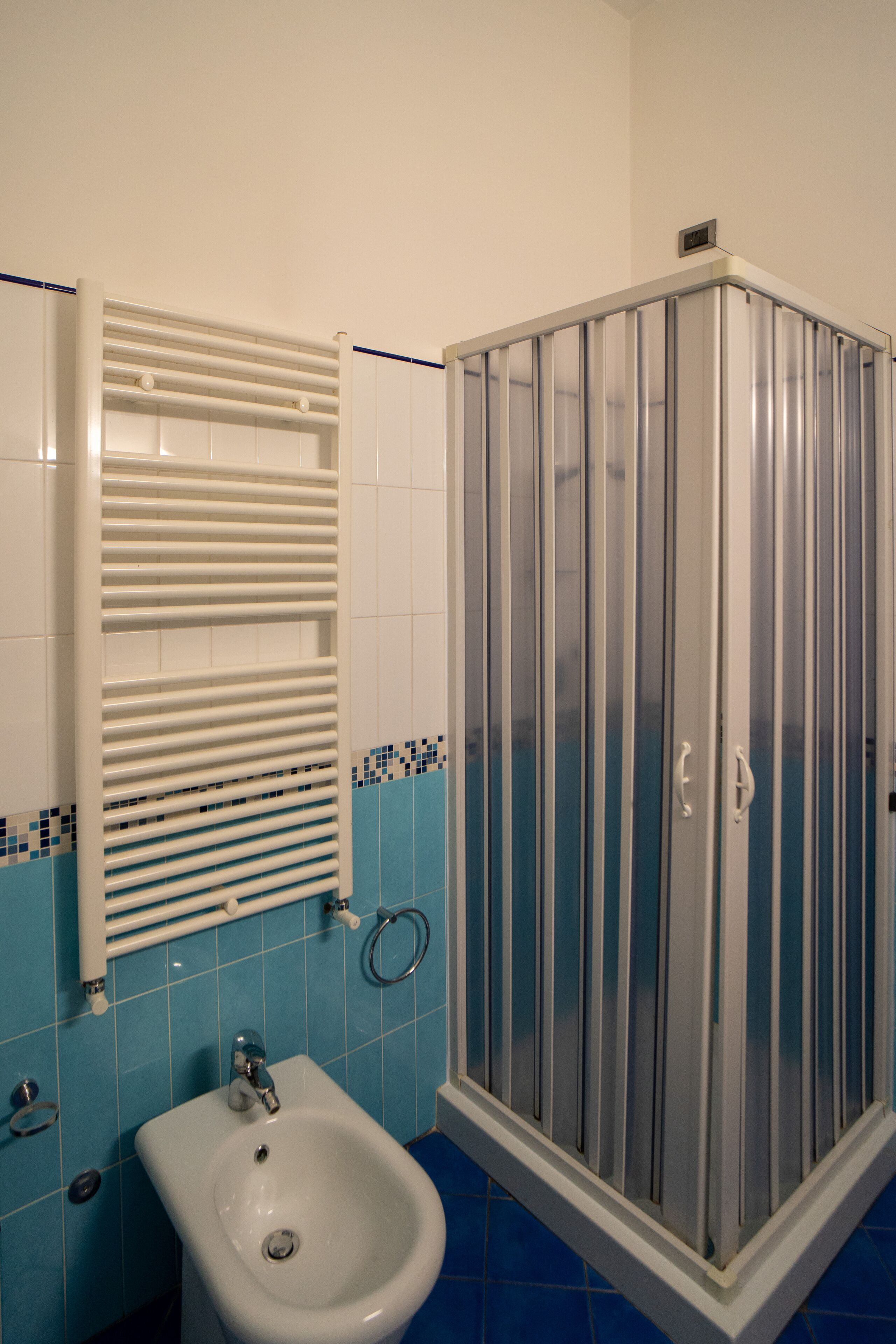 Ein Badezimmer mit einem weißen Waschbecken, blautonierten Fliesen und einer Duschkabine aus Glas.