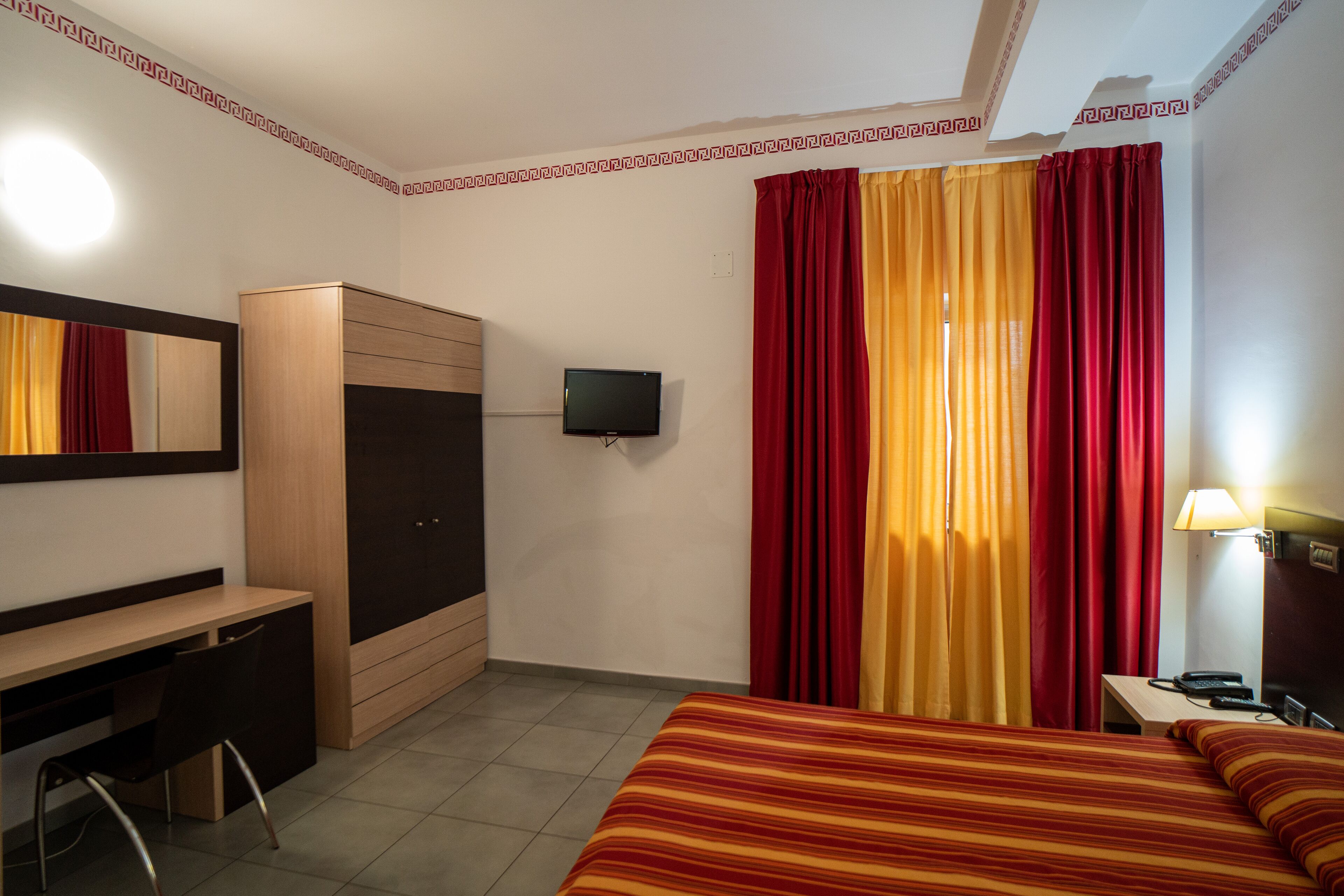 Ein Hotelzimmer mit Bett, Schreibtisch, Kleiderschrank, Fernseher und Vorhängen.