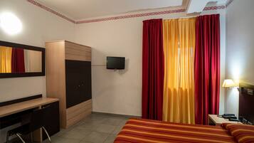 Ein Hotelzimmer mit Bett, Schreibtisch, Kleiderschrank, Fernseher und Vorhängen.