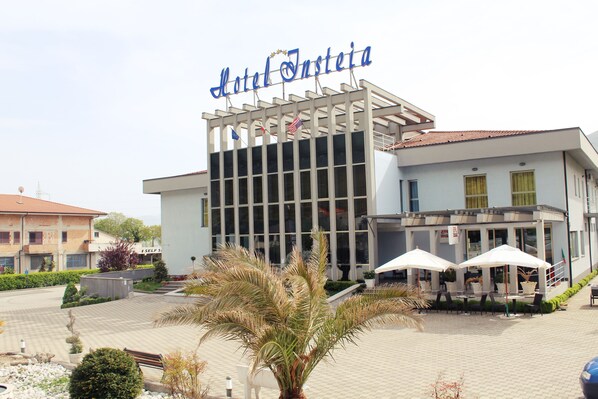 A hotel with a modern facade, a prominent sign, and outdoor seating with umbrellas.