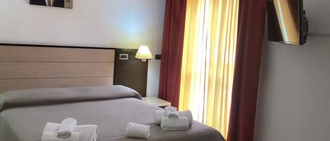 A hotel room with a large bed, two pillows, a nightstand with a lamp, a flat-screen TV, and a painting on the wall.