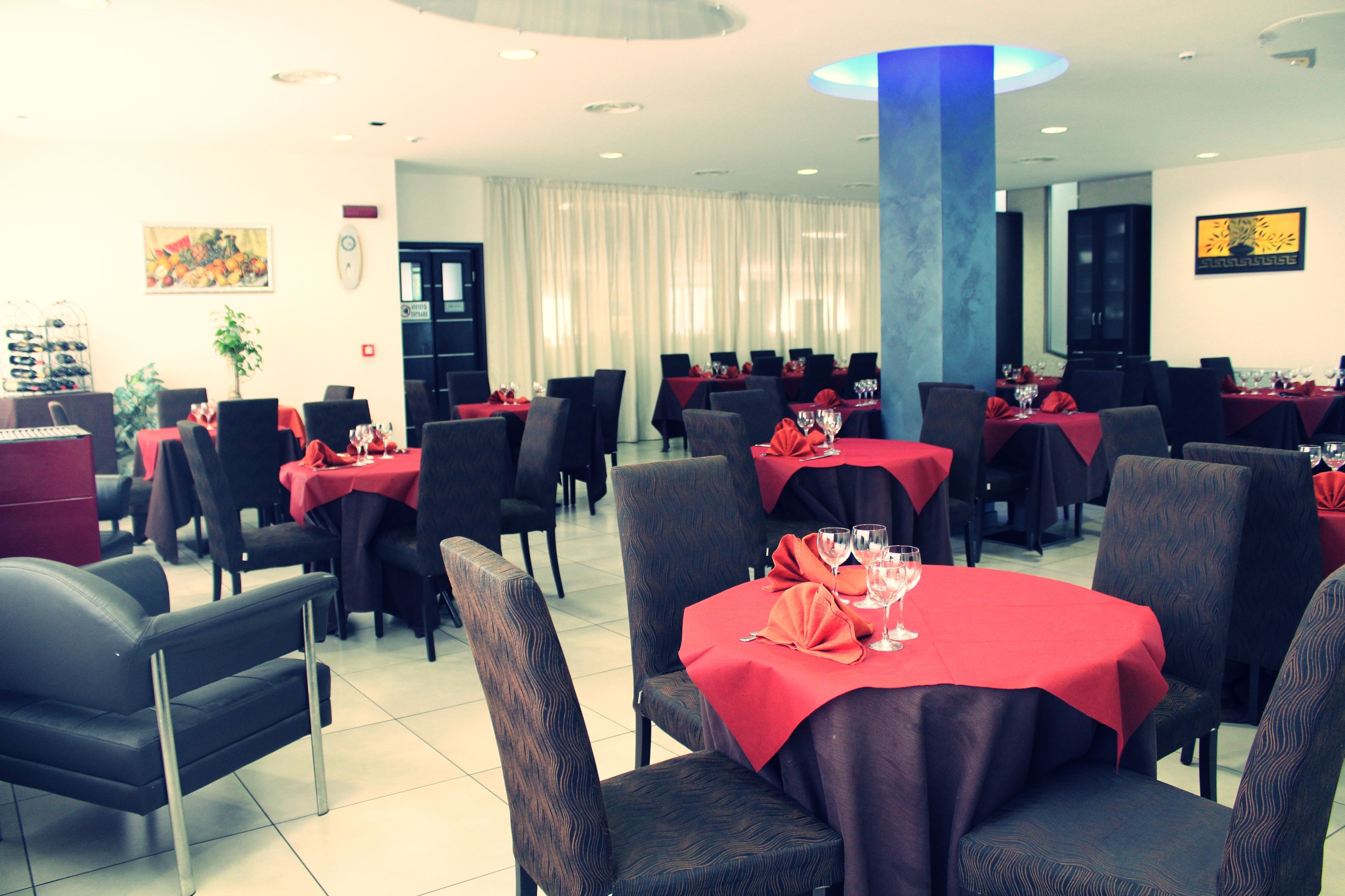 Un restaurant doté de nombreuses tables recouvertes de nappes rouges, disposées dans un espace vaste et agrémenté de chaises sombres.