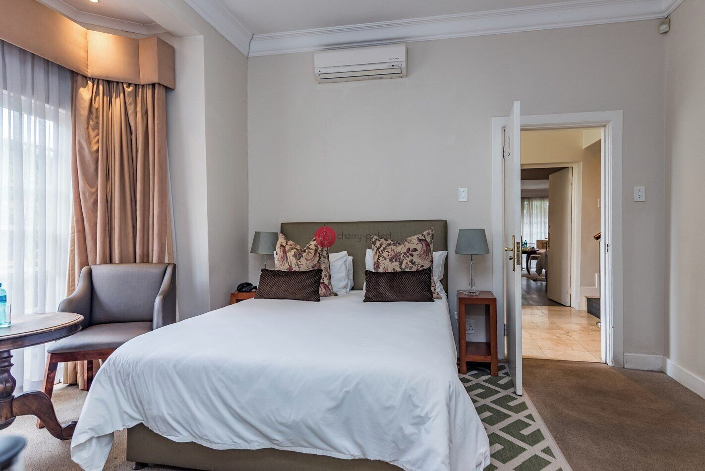 Ein Hotelzimmer mit einem großen Bett, einem Sessel, einem Nachttisch und einer Klimaanlage an der Wand.