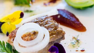A plate with a piece of meat, vegetables, and flowers.