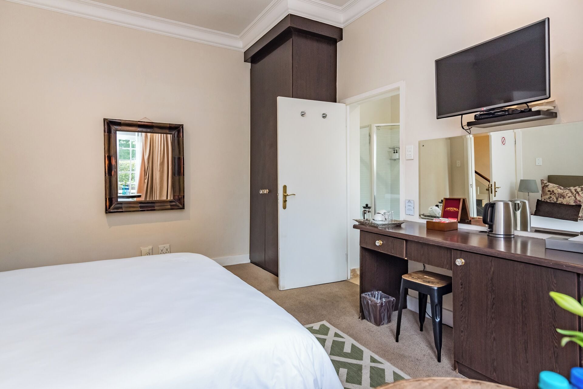Una habitación de hotel con cama, cómoda, espejo, televisión y un taburete pequeño.