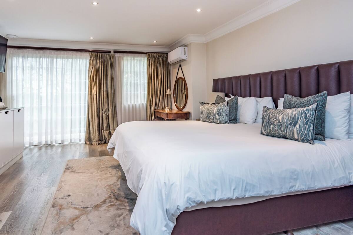 A modern bedroom with a large bed, a wooden nightstand, a mirror, and a ceiling fan.