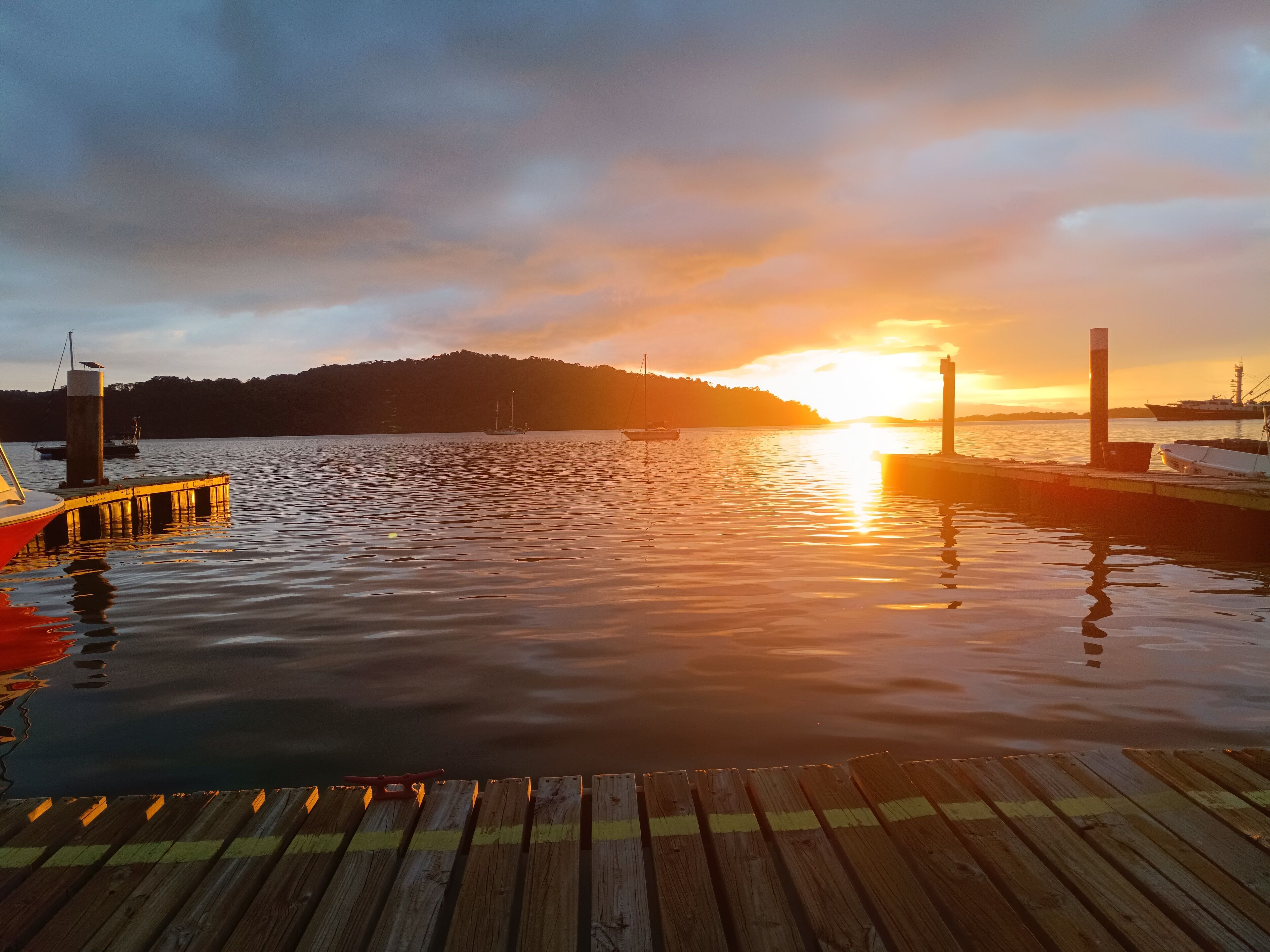 Een houten steiger die uitkomt op kalm water, met een zonsondergang op de achtergrond.
