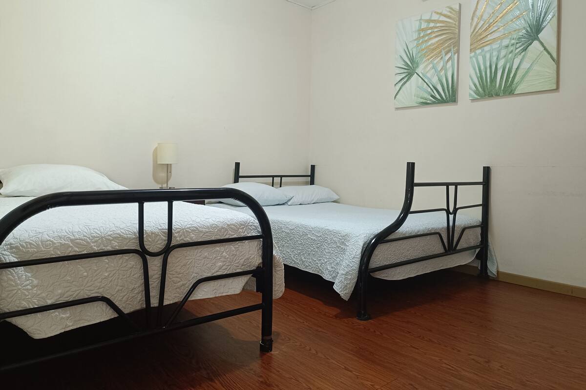 A room with two beds, a wall-mounted air conditioner, and two wall art pieces.