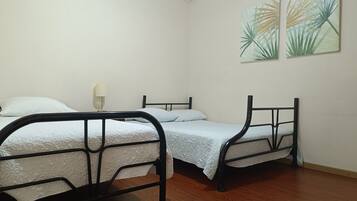 Een kamer met twee bedden, een wandairconditioner en twee decoratieve wandschilderingen.