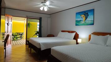 Habitación de hotel con dos camas, un ventilador de techo, un cuadro de un pájaro y vistas a un cuarto amarillo con kayaks.