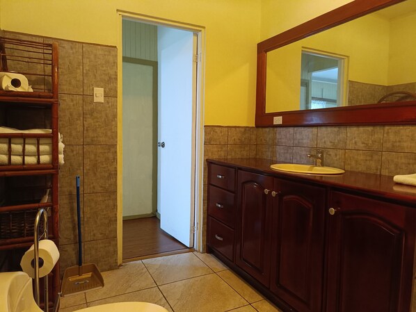 A bathroom with a wooden vanity, a sink, and a mirror. There is a door leading to another room.