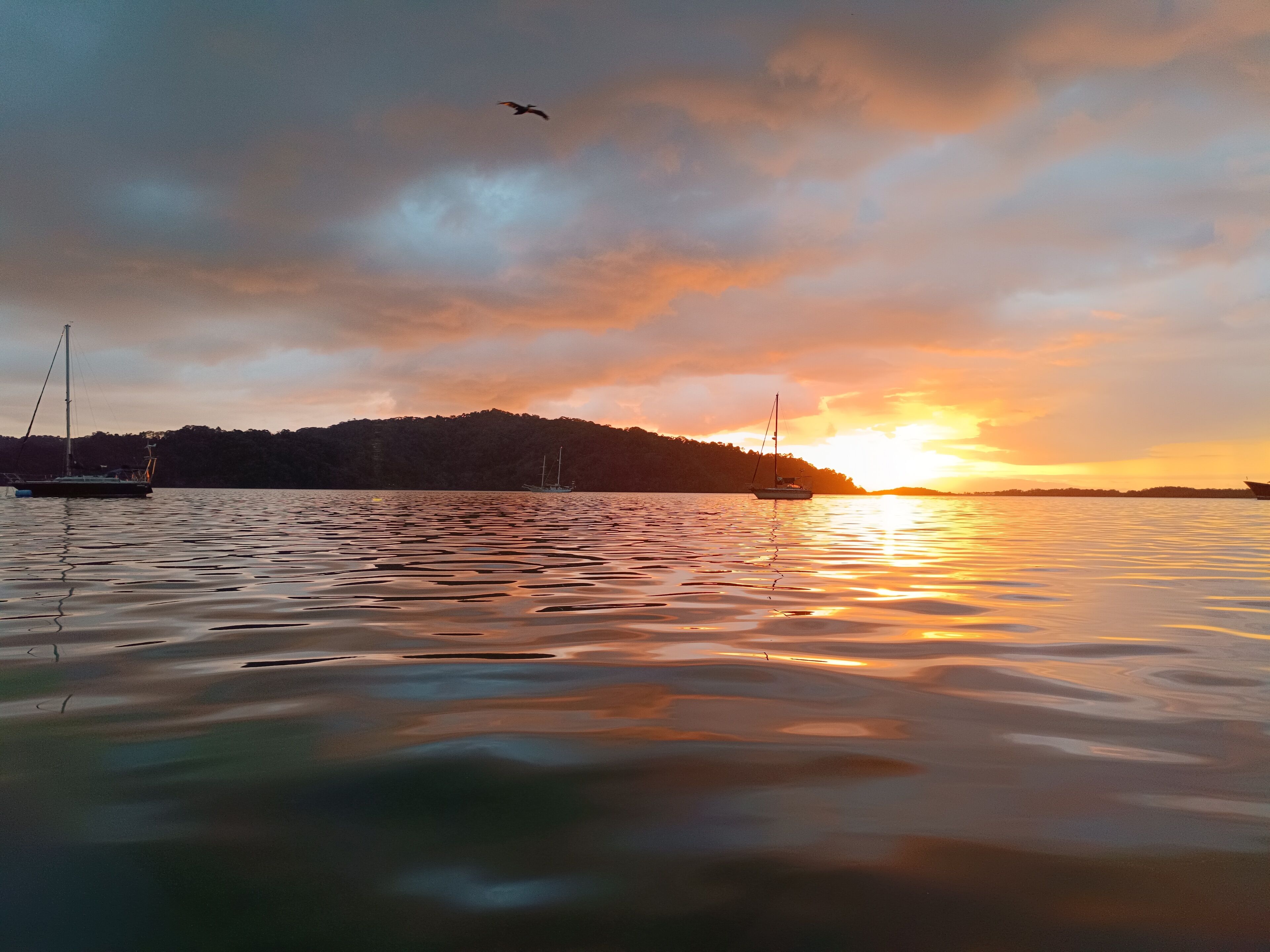 A calm lake at sunset with boats and a forested hill in the background.