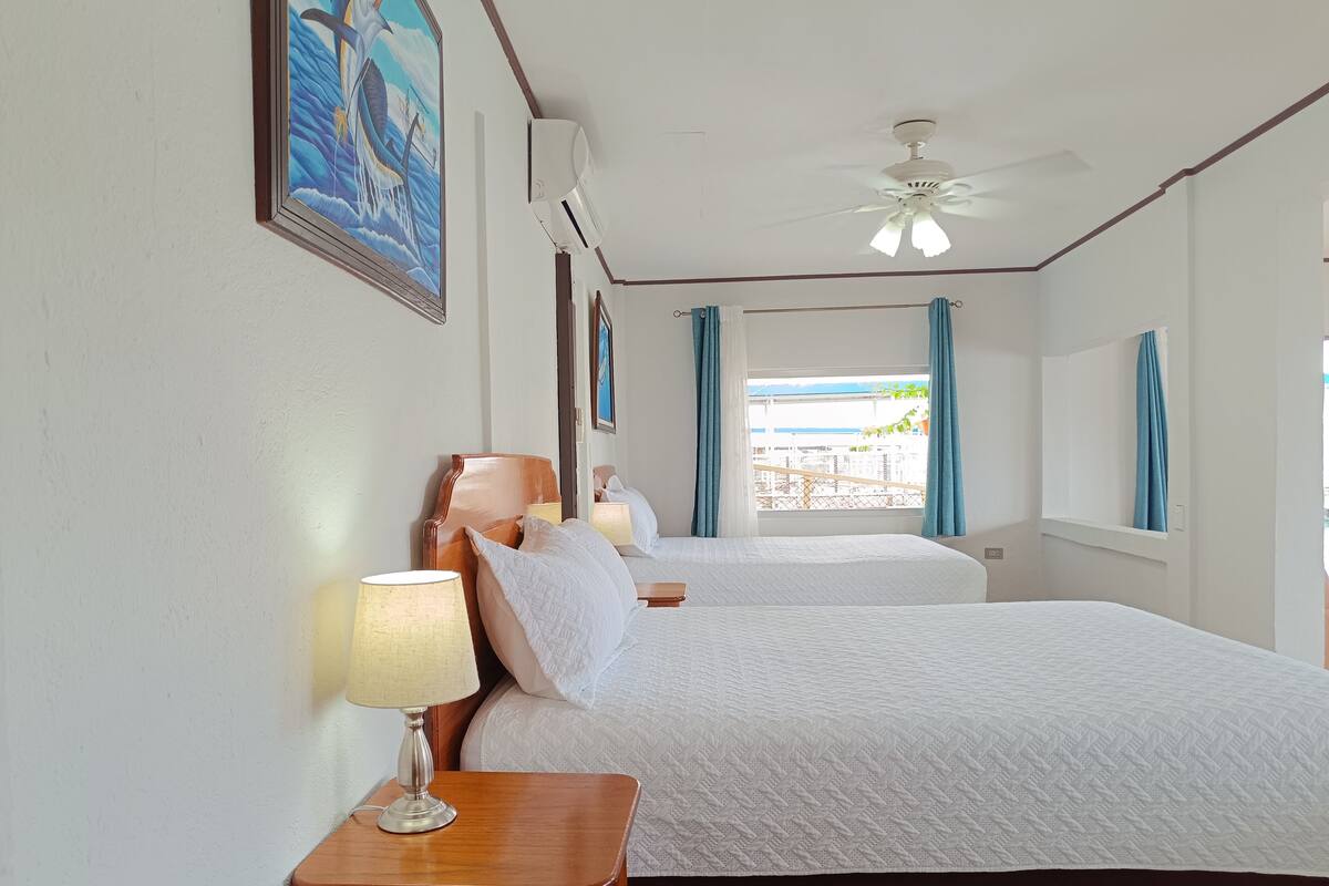 A hotel room with two beds, a ceiling fan, and a window with curtains.