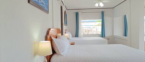 Quarto de hotel com duas camas, um ventilador de teto e uma janela com cortinas.