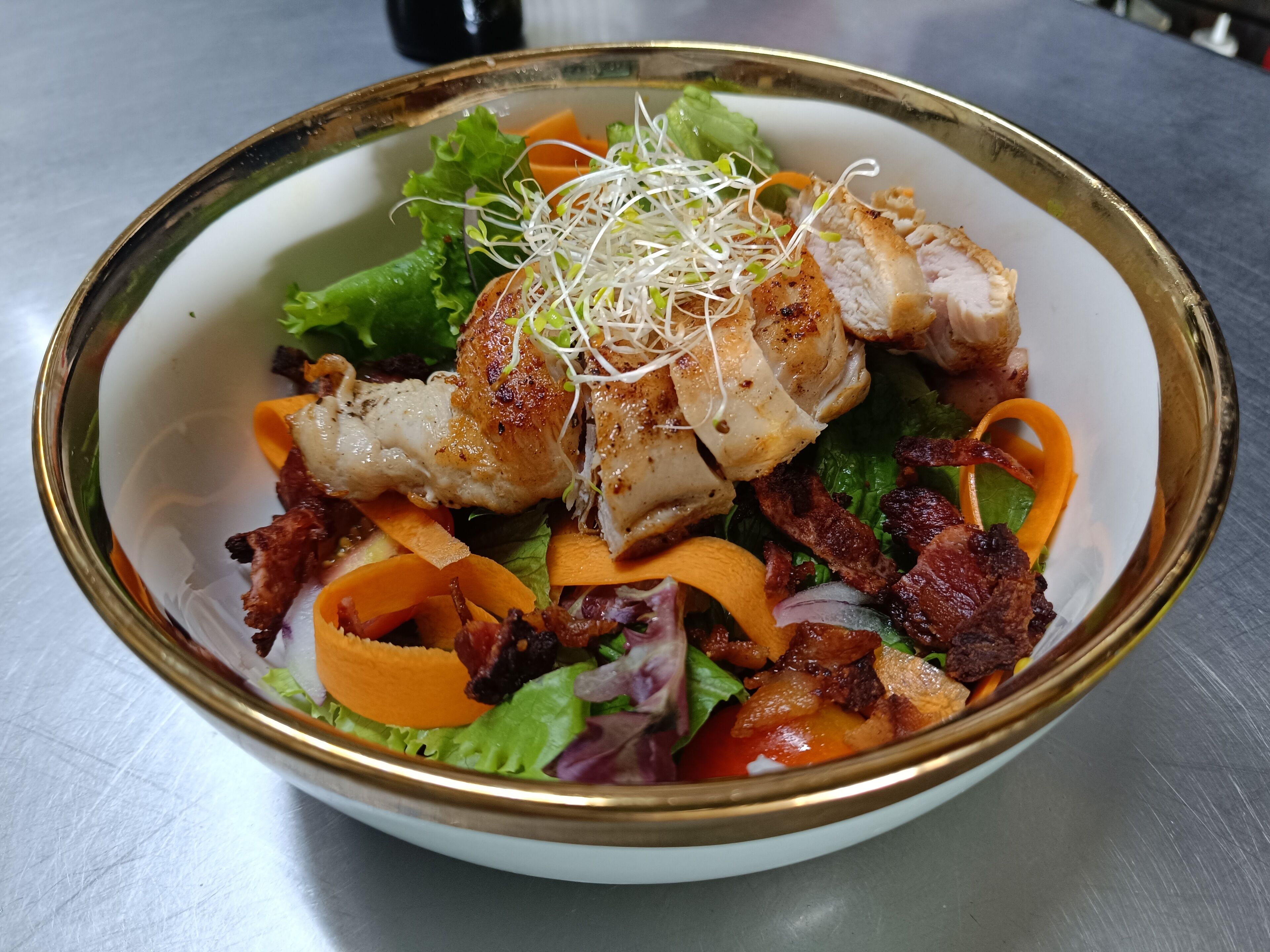 Un tazón de ensalada con lechuga, zanahorias, brotes y trozos de carne.