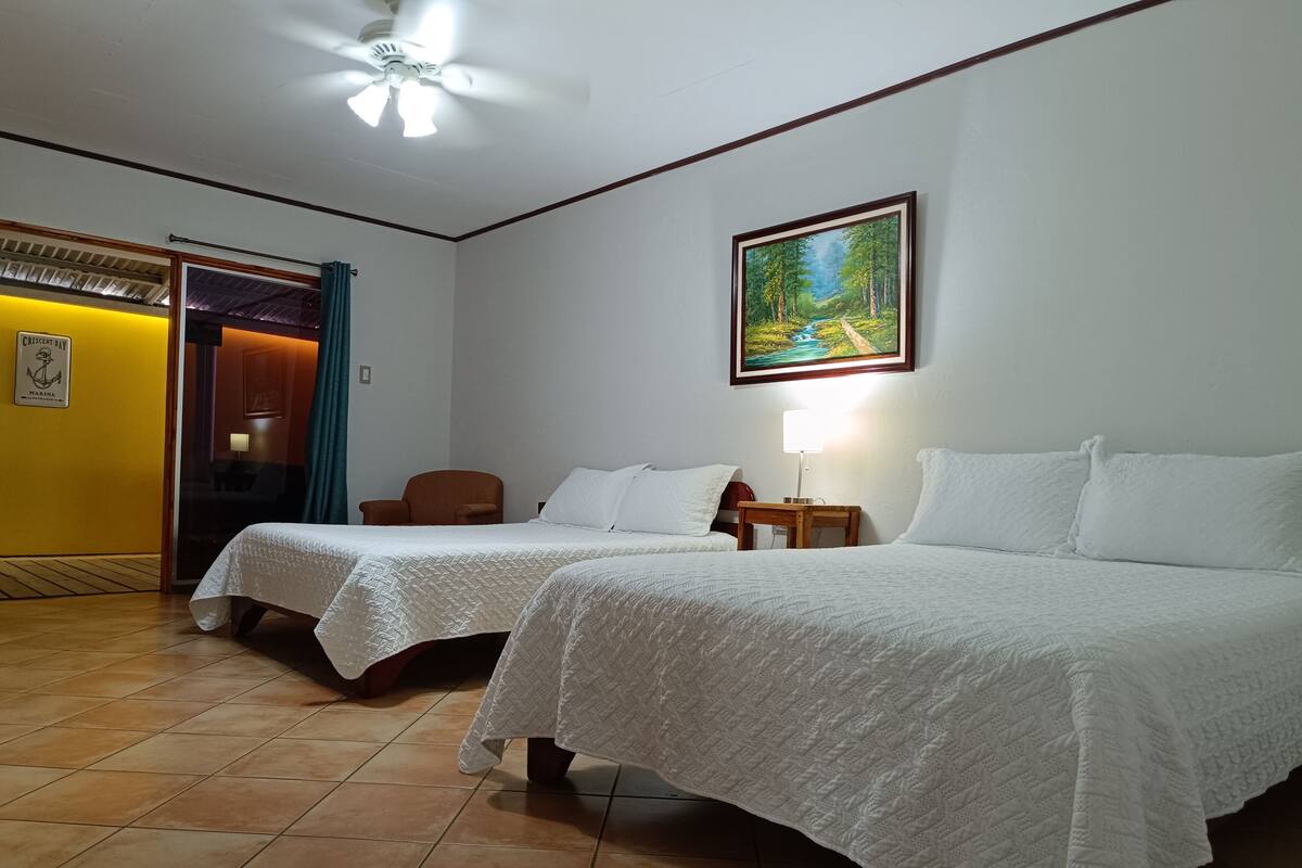 A hotel room with two beds, a painting on the wall, a ceiling fan, and a sign on the door.