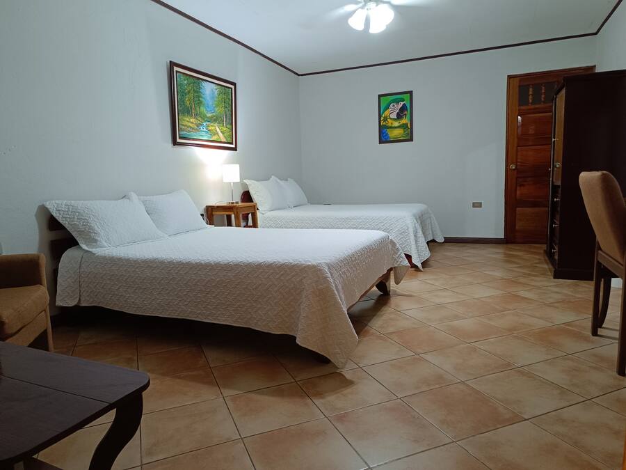 A room with two beds, a wooden table, a chair, a lamp, and a door.