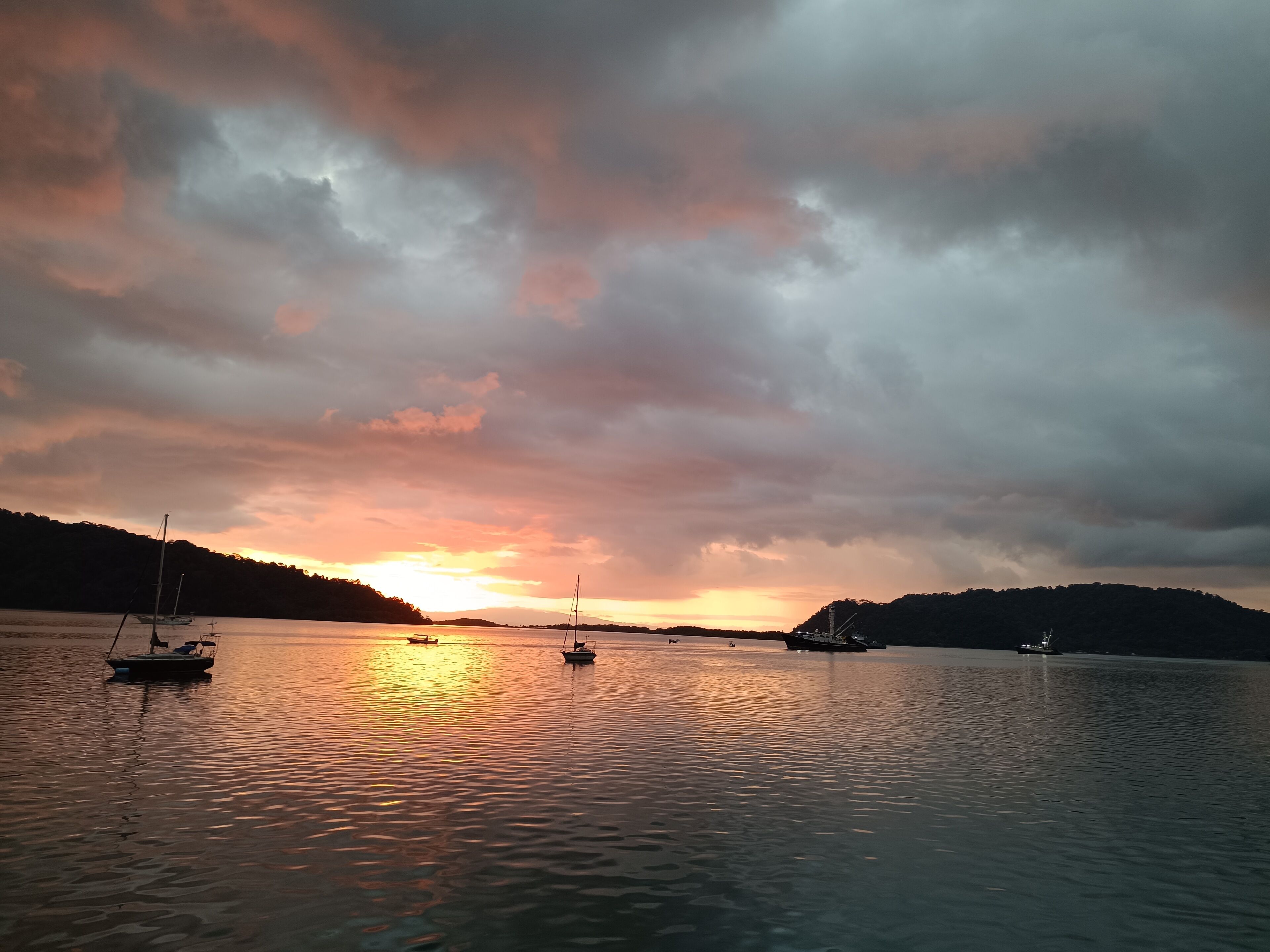 Un lago calmo al tramonto, con barche e colline sullo sfondo.