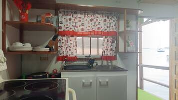 A kitchen with a stove, sink, and shelves with dishes.