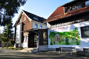 A building with a mural depicting outdoor scenes, a bench, and a clear sky. - Hotel & Hostel Drei Bären (Clausthal-Zellerfeld)