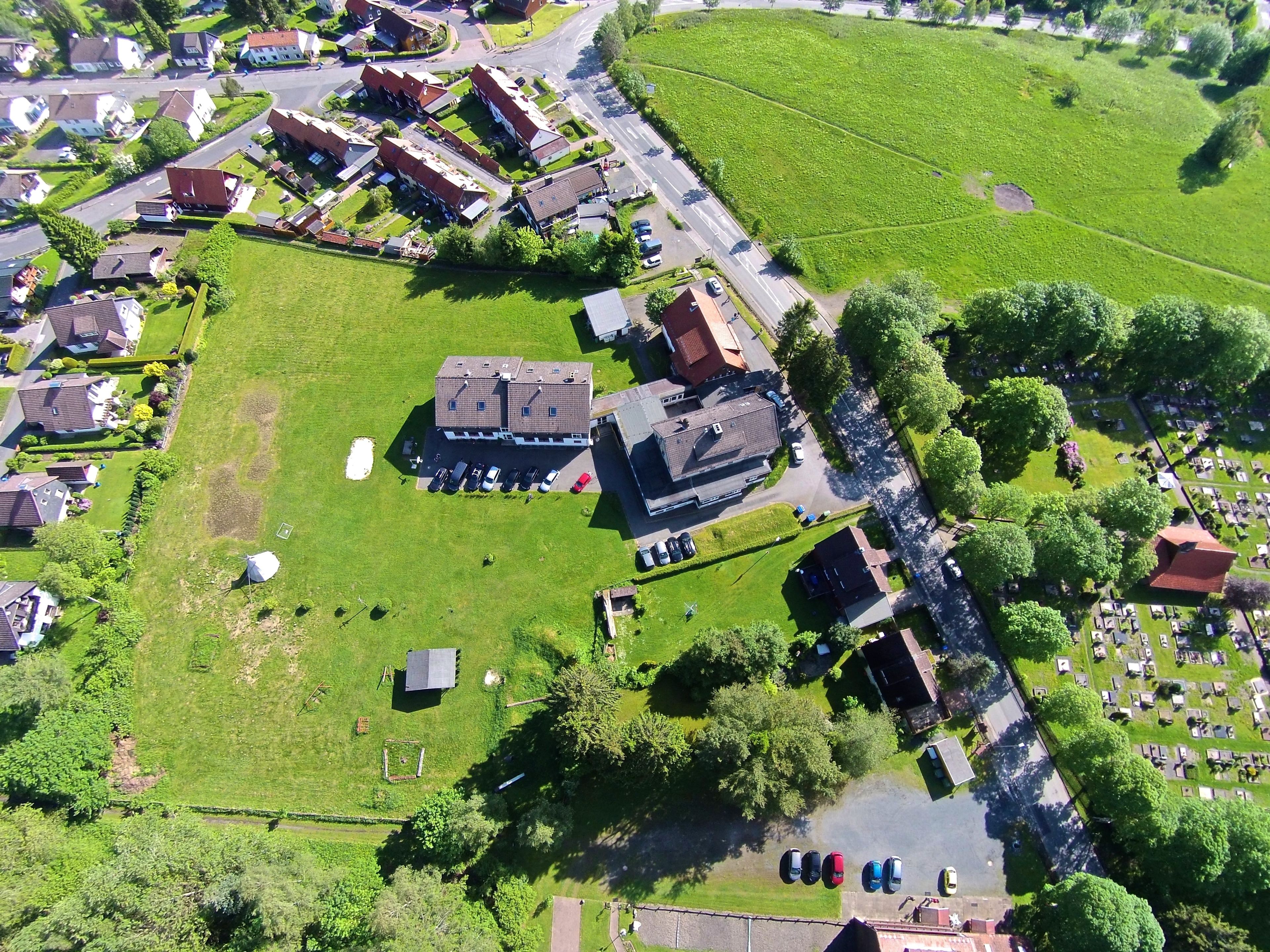 An aerial view of a residential area with houses, a large building with a parking lot, and a cemetery.
