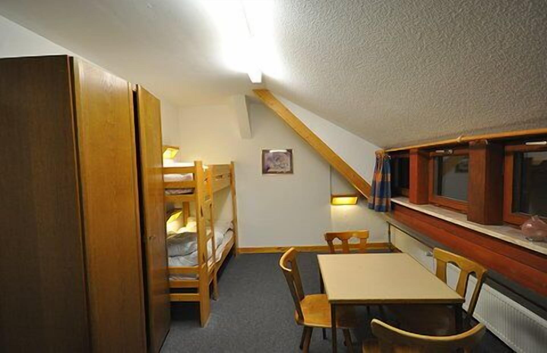 Una habitación pequeña y acogedora con literas, una mesa, sillas y un ventanal con cortinas.