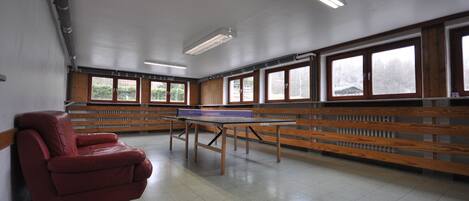 Una habitación con mesa de ping pong, bancos de madera y ventanas amplias.