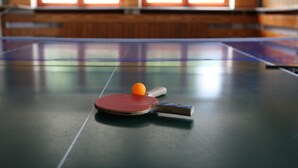 Tafeltennistafel met een racket en bal in een kamer met houten lambrisering en een raam.