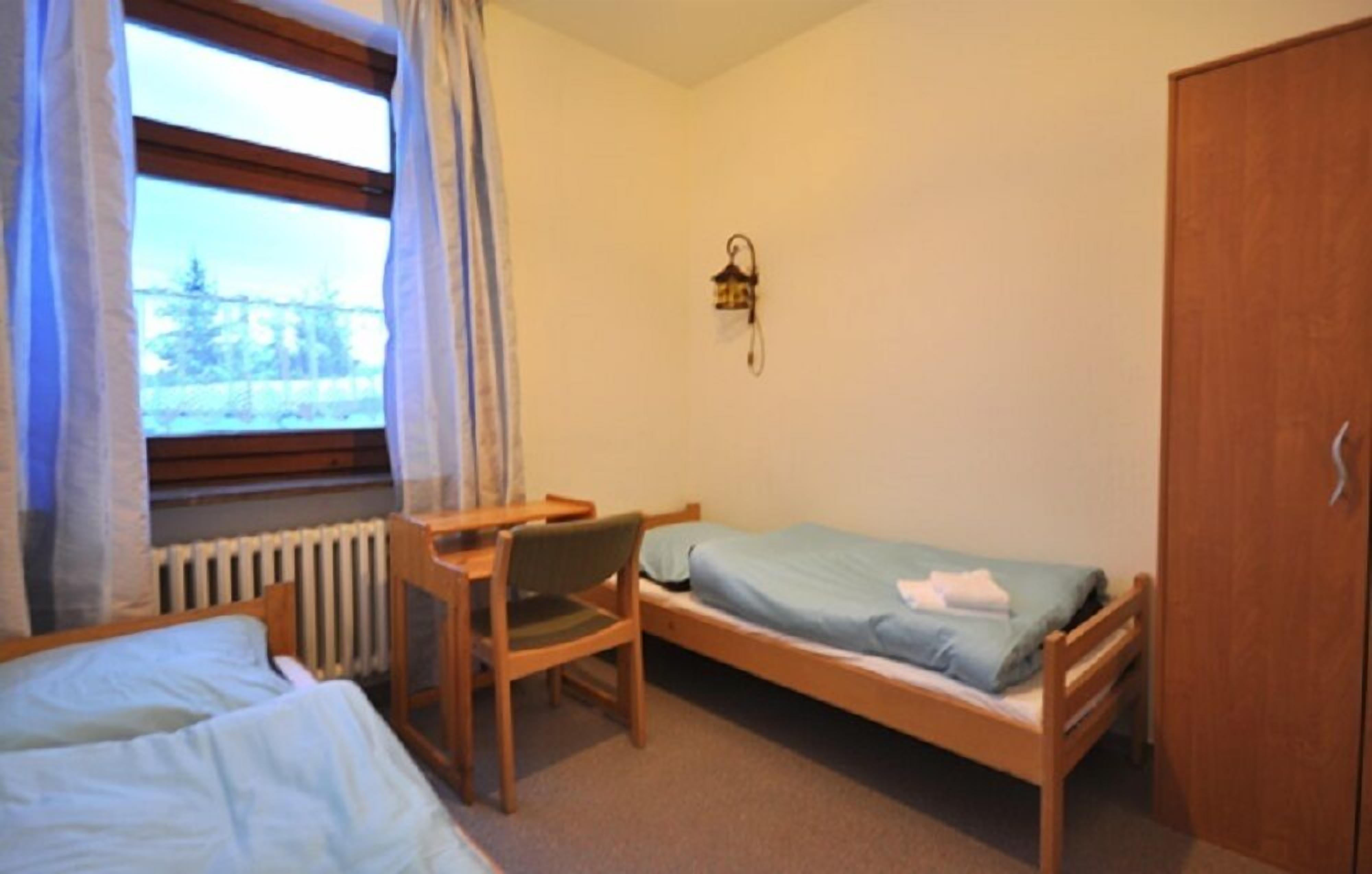 A small room with two single beds, a wooden desk, a chair, a radiator, and a wardrobe.