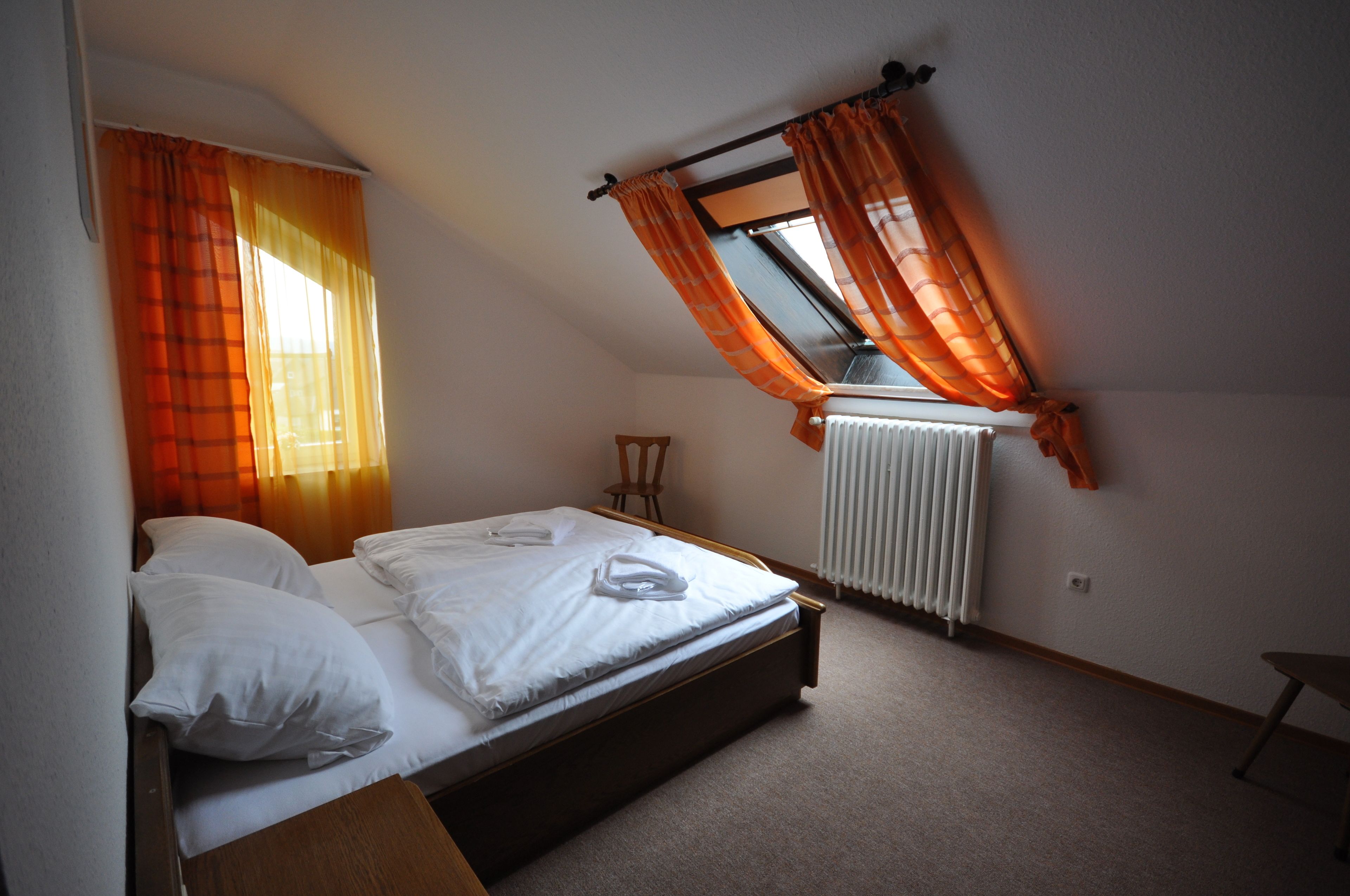 A bedroom with a bed, a window with curtains, a radiator, and a small table.