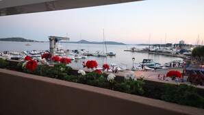 A marina with boats docked, a small island in the background, and a view through a balcony with red flowers. - SCALA Bed & Breakfast (Vodice)