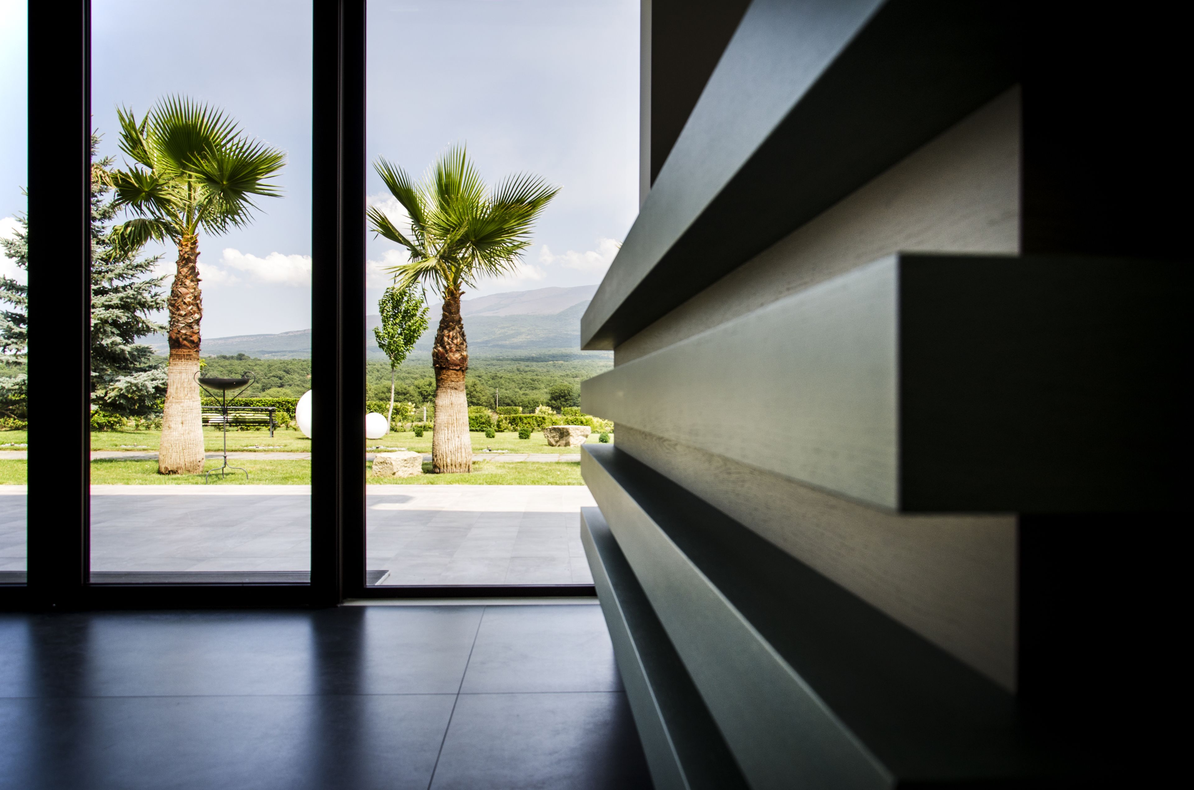 A modern interior with a view of palm trees and a landscaped garden.