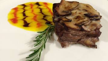 A plate with a piece of meat topped with mushrooms and a yellow sauce with a red pattern.